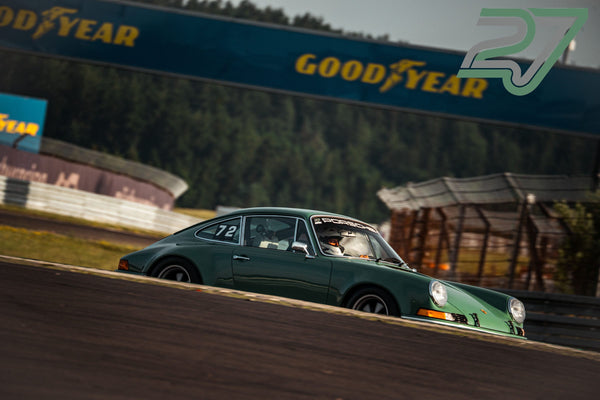 Dunkelgrüner klassischer Porsche 911 mit Fahrer im Helm zieht scharf gezeichnet durch eine Kurve am Nürburgring