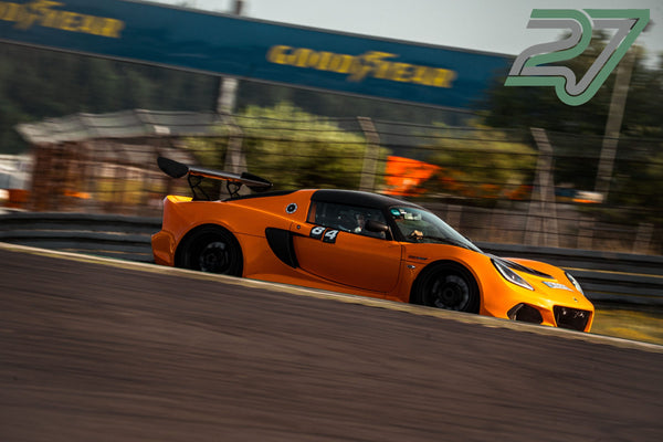 Oranger Lotus Exige mit großem Heckflügel zieht im Seitenprofil an der Kamera vorbei