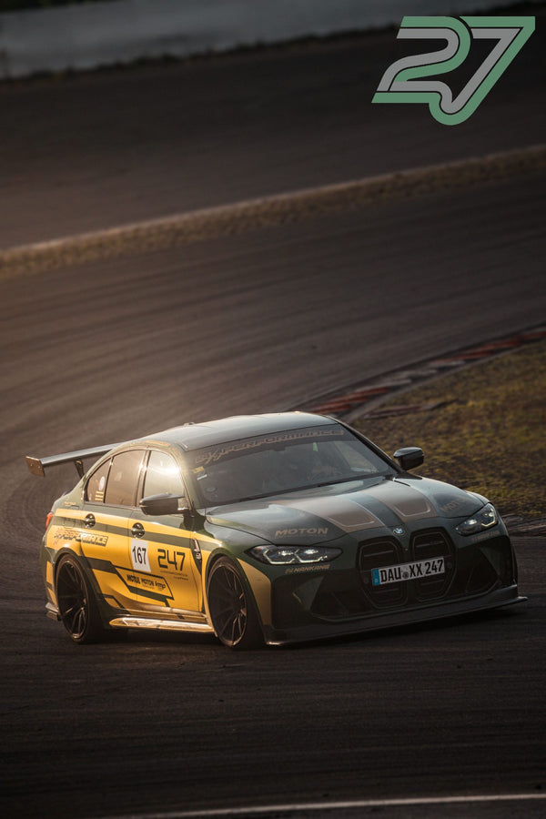 Grün-goldener BMW M3 fährt mit eingeschalteten Scheinwerfern aus einer Kurve auf die Kamera zu