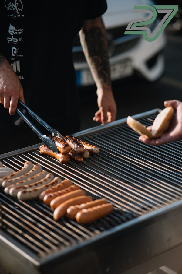 Zwei Hände wenden Bratwürste und Würstchen mit einer Grillzange auf dem Fahrerlager-Grill