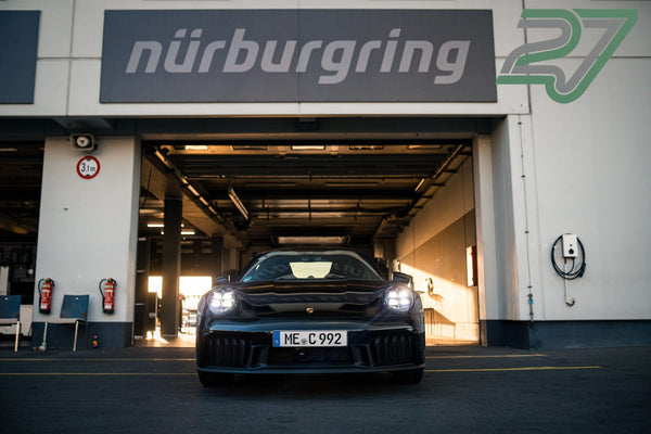 Schwarzer Porsche 911 fährt mit Scheinwerfern durch das Boxentor mit dem Schriftzug nürburgring