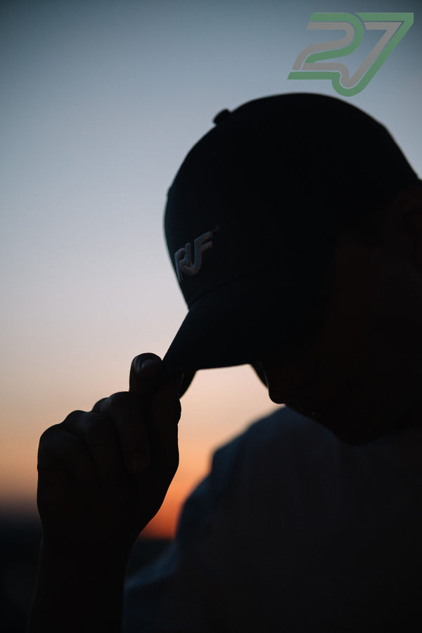 Silhouette einer Person zupft die Kappe zurecht vor orange-blauem Abendhimmel