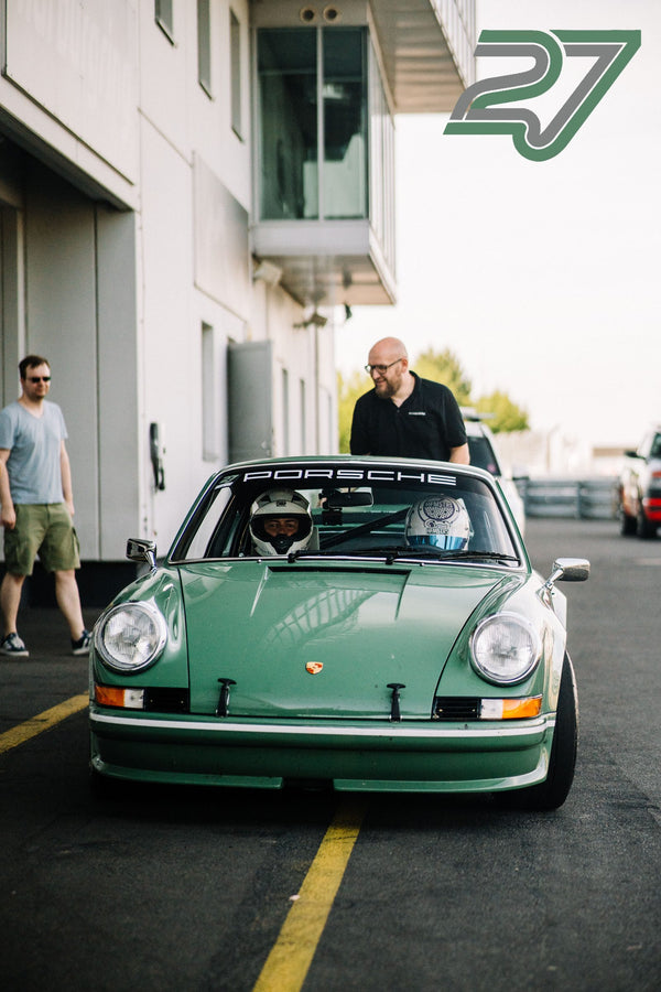 Mintgrüner klassischer Porsche 911 rollt mit Helm tragendem Fahrer durch die Boxengasse