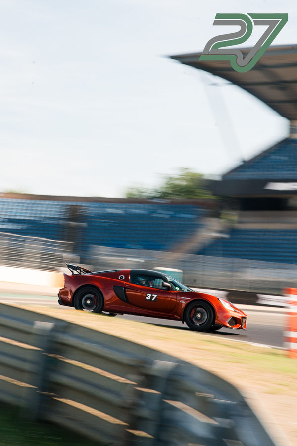 Dunkelroter Lotus Exige fährt mit Bewegungsunschärfe schnell durch eine Kurve der Strecke