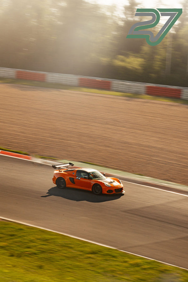 Oranger Lotus Exige rast mit Bewegungsunschärfe durch eine Kurve im diesigen Gegenlicht