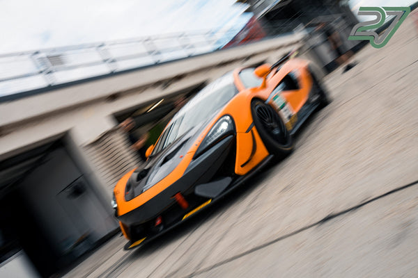 Orange-schwarzer McLaren-Rennwagen rast mit starker Bewegungsunschärfe an der Boxenmauer vorbei