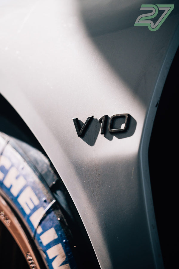 Nahaufnahme des V10-Schriftzugs am Kotflügel, im Hintergrund ein Michelin-Reifen