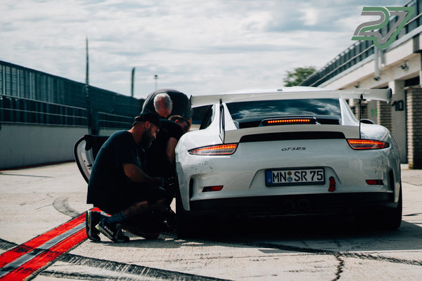 Mehrere Männer beugen sich über das Heck eines weißen Porsche 911 GT3 RS in der Box
