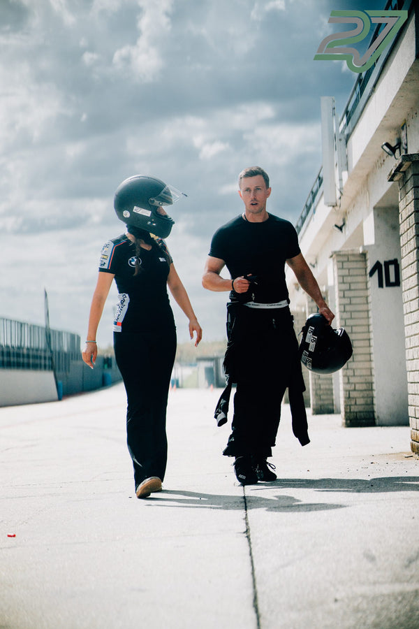 Frau mit Helm und BMW-Shirt geht neben einem Mann, der zwei Helme trägt, durch die Boxengasse