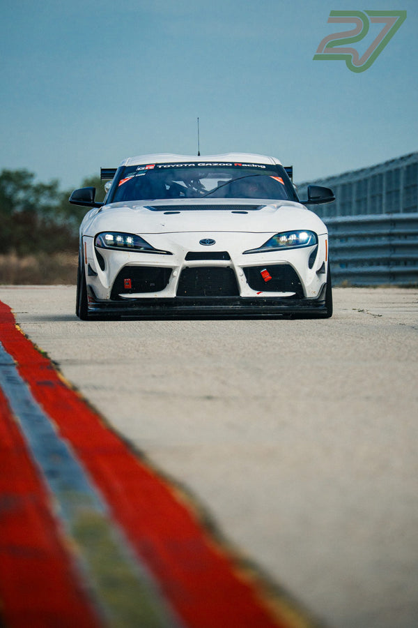 Weißer Toyota Supra von Toyota Gazoo Racing steht mit Scheinwerferlicht auf dem Asphalt, blauer Himmel