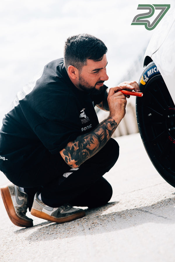 Tätowierter Mechaniker markiert kniend einen Michelin-Reifen mit einem orangen Stift
