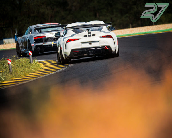 Weißer Toyota Supra führt vor grauem Audi durch die Kurve, beide dicht hintereinander