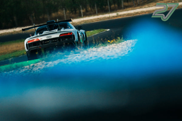 Grauer Audi R8 zieht mit Wasserspritzern aus der Kurve, im Vordergrund verschwommenes Blau