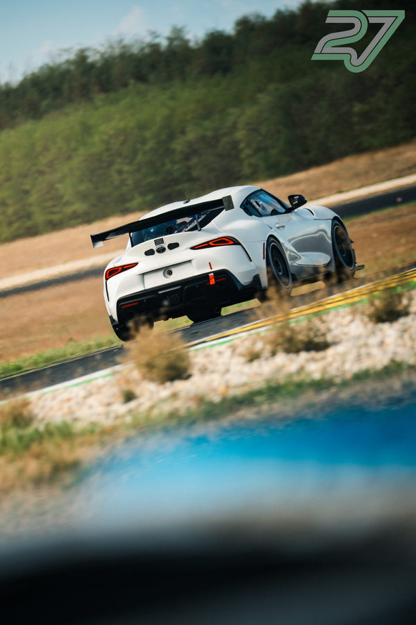 Weißer Toyota Supra hüpft von hinten gesehen über einen Curb, Unschärfe im Vordergrund