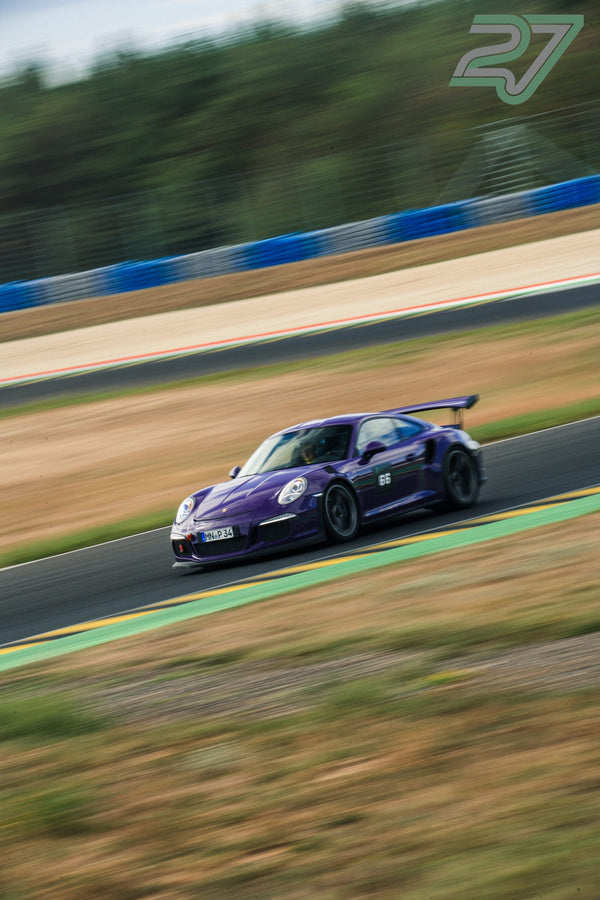 Violetter Porsche 911 GT3 mit Fahrer im Helm fährt durch eine weite Kurve, Landschaft stark verwischt
