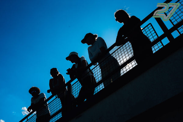 Fünf Personen lehnen als Silhouetten vor blauem Himmel an einem Geländer im Gegenlicht