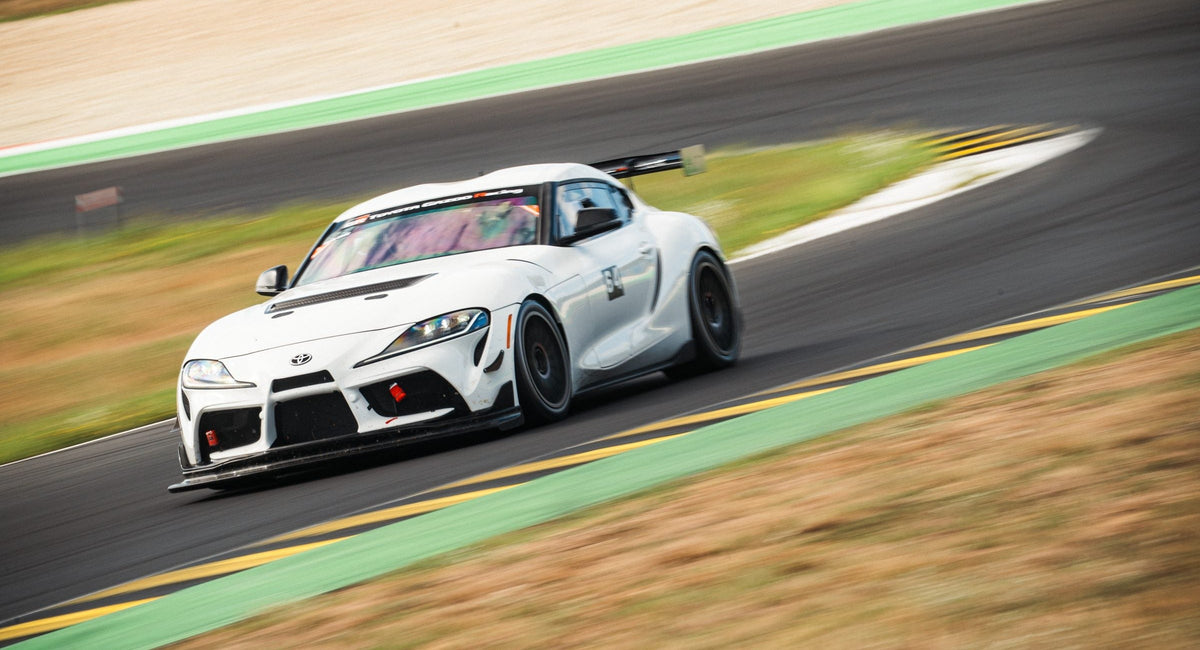 White Toyota Supra race car cornering through a fast section with strong motion blur at the Pannonia-Ring
