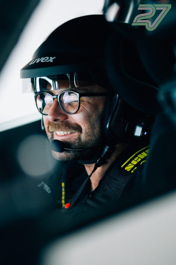 Fahrer mit Uvex-Helm, Brille und Headset lacht breit und blickt konzentriert zur Seite