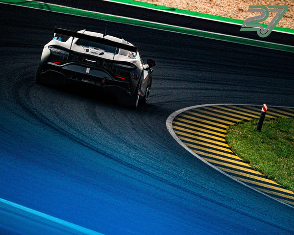 Weißer McLaren beschleunigt aus einer Kurve, im Vordergrund verschwommenes Blau