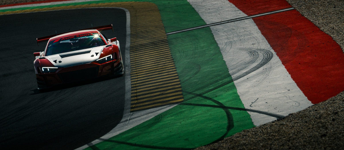 Rot-weißer Audi R8 GT3 kurvt aus der Vogelperspektive über den rot-weiß-grünen Curb am Pannonia-Ring