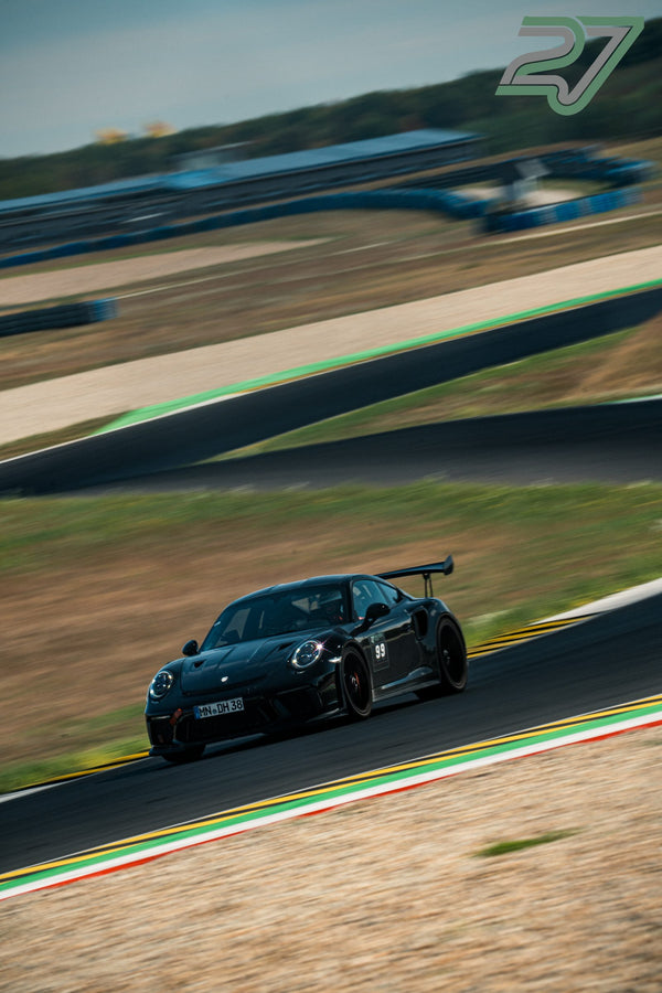 Schwarzer Porsche 911 GT3 fährt konzentriert eine sanfte Kurve, Streckenpanorama im Hintergrund