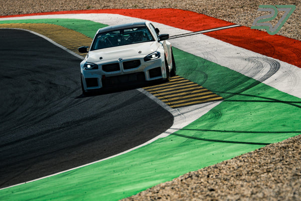 Weißer BMW M2 Rennwagen lenkt stark ein und rollt über den farbigen Curb einer engen Kurve