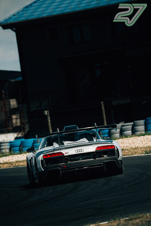 Weißer Audi R8 fährt von hinten fotografiert vor einem dunklen Gebäude im starken Kontrastlicht