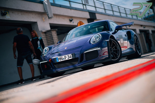 Bläulich-violetter Porsche 911 GT3 steht in der Boxengasse, im Hintergrund unterhalten sich zwei Personen