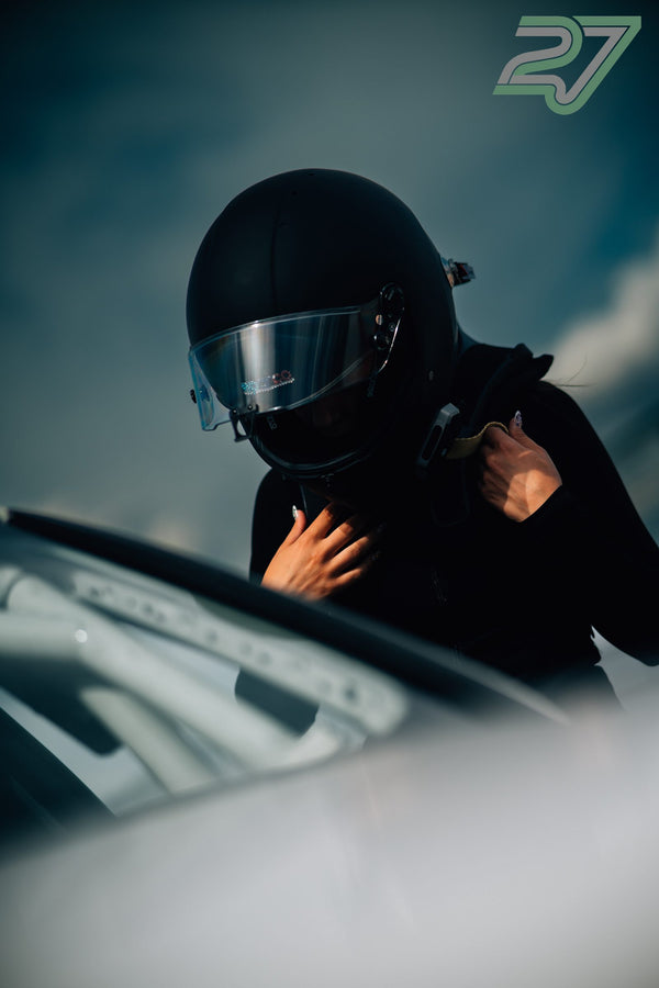 Fahrerin mit dunklem Helm und geschlossenem Visier schnallt neben dem Auto den Kinnriemen fest