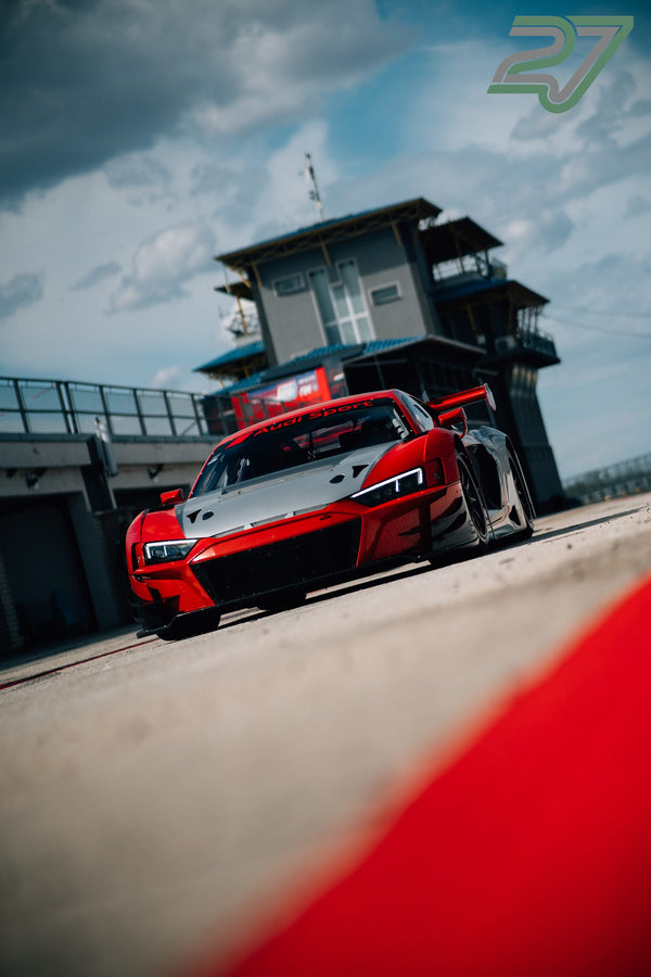 Rot-weißer Audi R8 GT3 steht schräg von unten fotografiert vor dem Rennkontrollturm im Abendlicht
