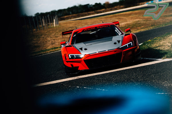 Rot-weißer Audi R8 GT3 fährt aggressiv durch eine Kurve, im Vordergrund eine verschwommene Silhouette