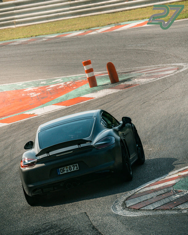 Anthrazitfarbener Porsche Cayman gleitet von oben gesehen durch die Schikane am Curb
