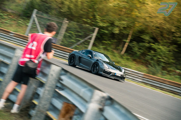 Ein Streckenposten in roter Weste beobachtet den vorbeifahrenden Porsche an der Leitplanke