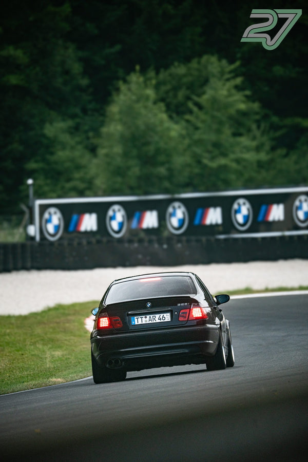 Schwarzer BMW 3er entfernt sich vor der BMW-M-Bannerwand, die Rücklichter leuchten rot