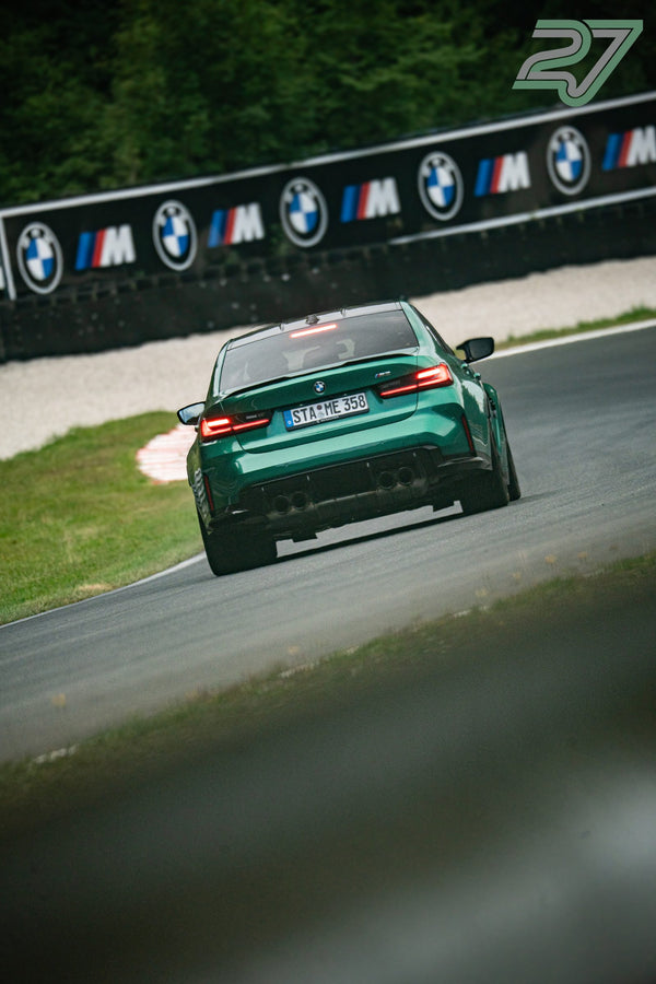 Dunkelgrüner BMW M3 entfernt sich langsam von der BMW-M-Bannerwand im dichten Wald