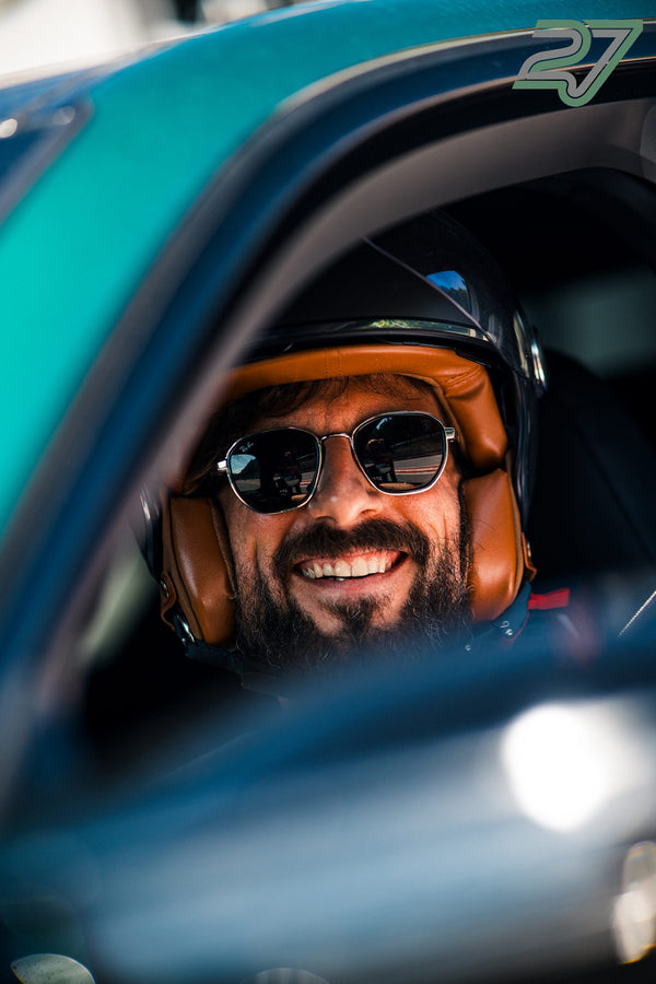 Bärtiger Fahrer lacht im türkisfarbenen Auto, schwarzer Helm mit cognacfarbenem Innenpolster