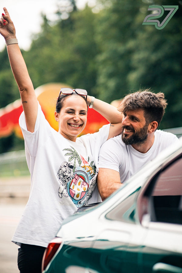 Eine Frau reckt lachend die Faust in die Luft, ein Mann steht lächelnd neben ihr am Auto