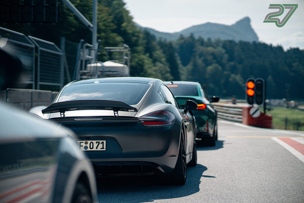 Mattgrauer Porsche mit breitem Heckflügel steht an der roten Ampel vor dem markanten Bergpanorama