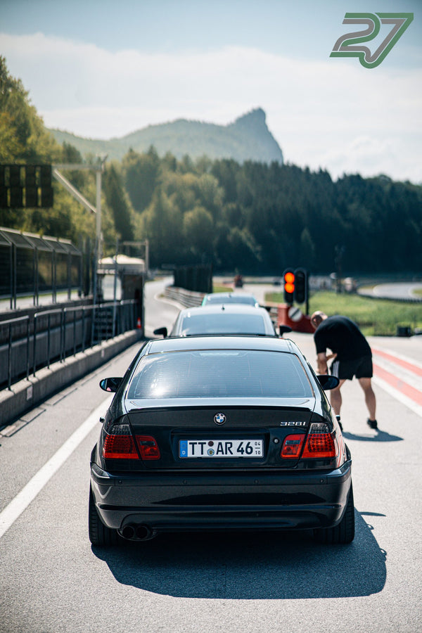 Schwarzer BMW 328i wartet an der Ampel, während sich ein Mann zur Fahrertür hinunterbeugt