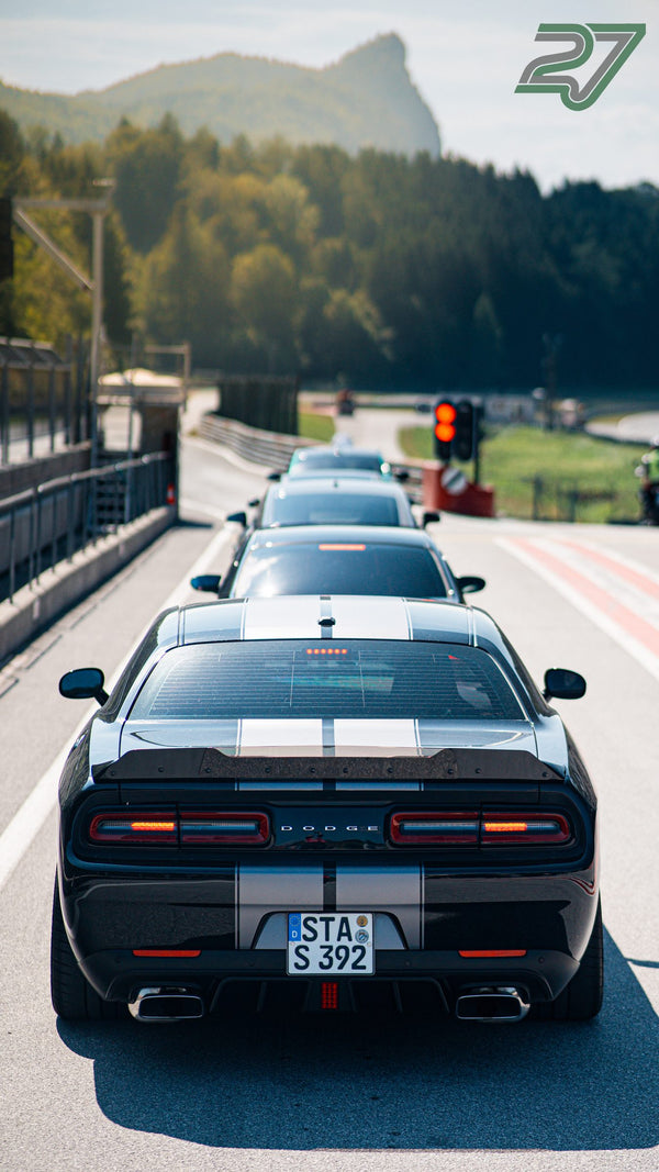 Schwarzer Dodge Challenger mit hellen Streifen rollt vor der Bergkulisse in die Warteschlange ein