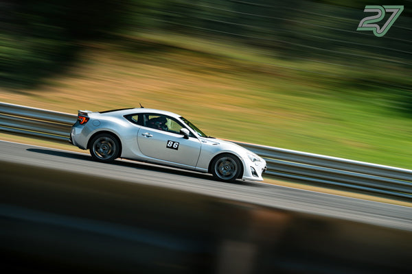 Silberner Toyota GT86 mit Startnummer 86 zieht in schneller Kurvenfahrt vorbei, Landschaft verwischt