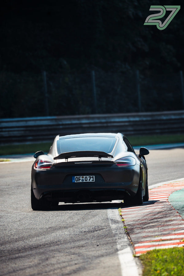 Mattgrauer Porsche mit großem Heckflügel fährt aus einer dunklen Schattenkurve heraus