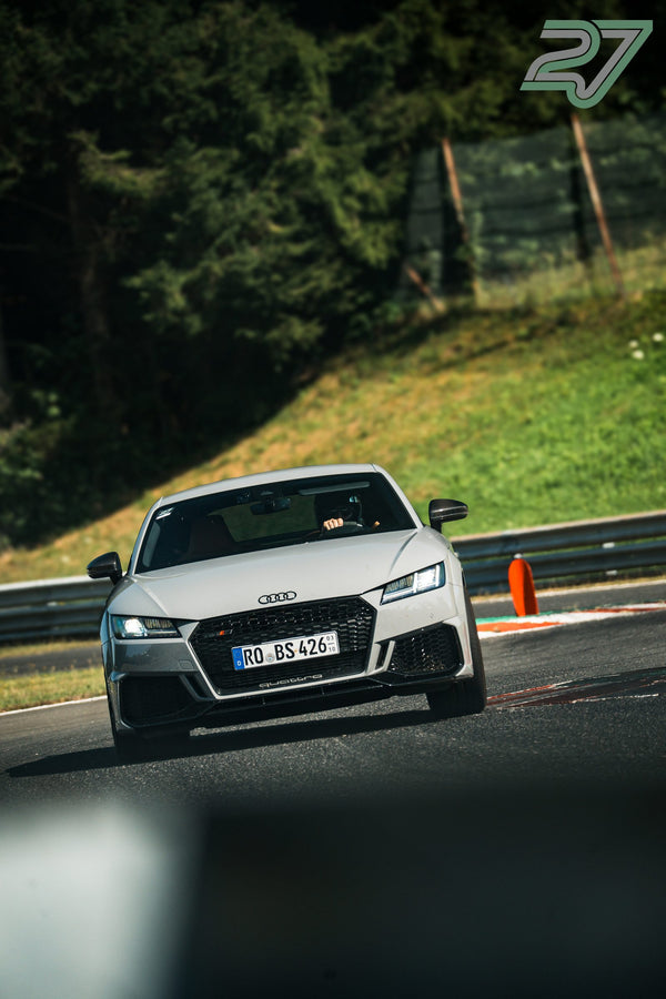 Hellgrauer Audi TT RS rollt im Sonnenlicht aus der Kurve, Wiese und Bäume im Hintergrund