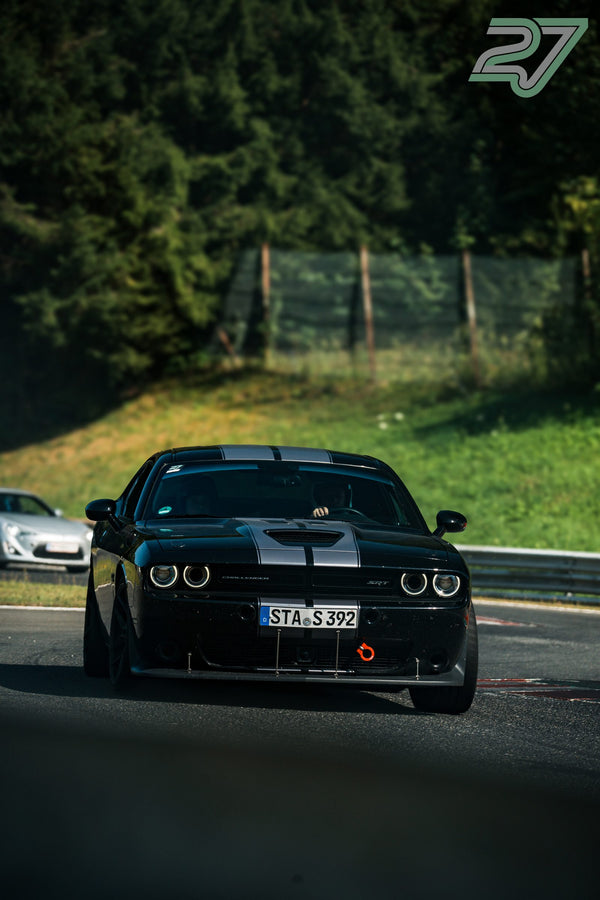 Schwarzer Dodge Challenger mit grauen Streifen durchfährt die Schattenkurve, dahinter ein silberner Toyota