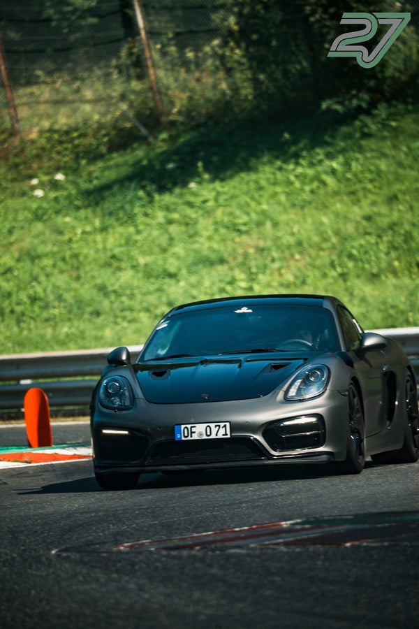 Anthrazitfarbener Porsche Cayman GT4 rollt im Schatten an einem orangen Pylon vorbei