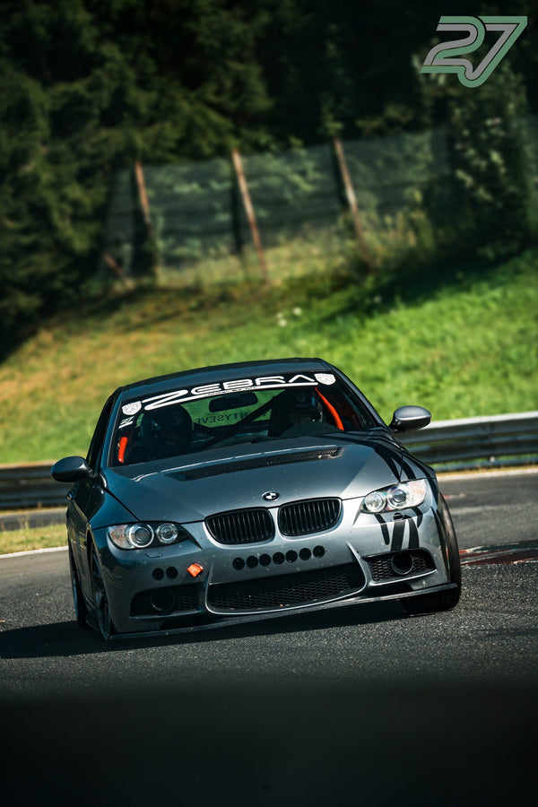 Grauer BMW 3er mit schwarzen Streifen-Decals kurvt sonnenbeschienen durch die Kurve, Käfig sichtbar