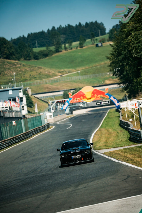 Schwarzer Dodge Challenger nähert sich unter blauem Himmel dem Red-Bull-Bogen am Hang