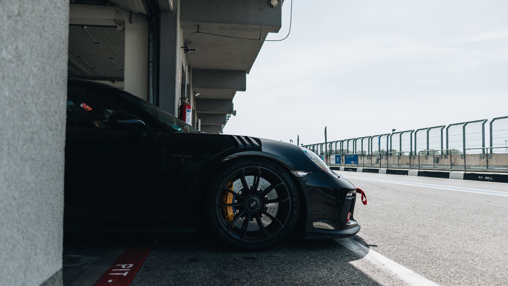 Schwarzer Porsche GT3 RS mit schwarzen Felgen und gelben Bremssätteln beim Einfahren in die Boxengasse einer Rennstrecke.