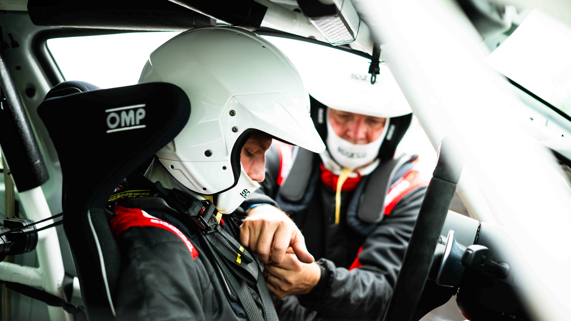 Vater und Sohn die sich bei einem Trackday gegenseitig helfen im Auto anzuschnallen.