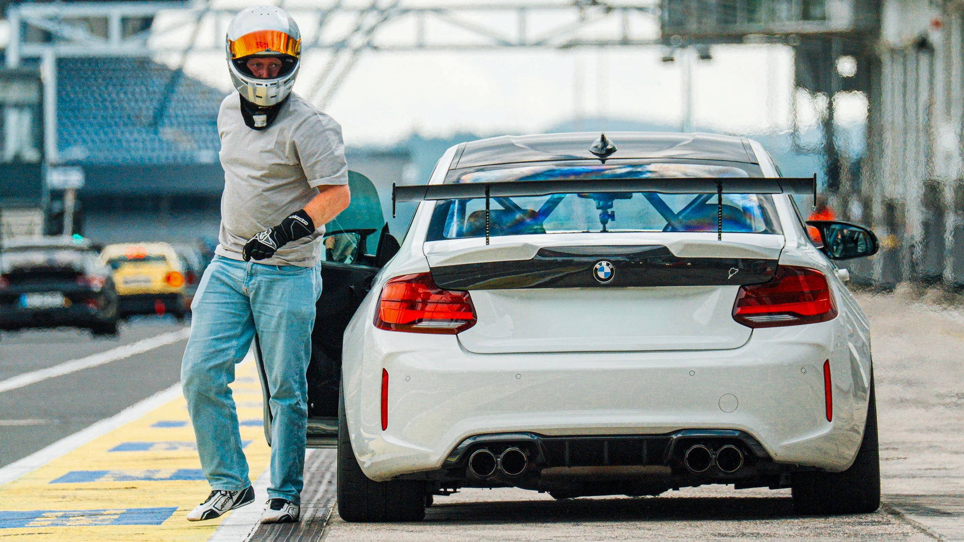 Fahrer mit einem Stilo ST5 GT Rennhelm neben seinem BMW M2 Tracktool in der Boxengasse des Nürburgrings.